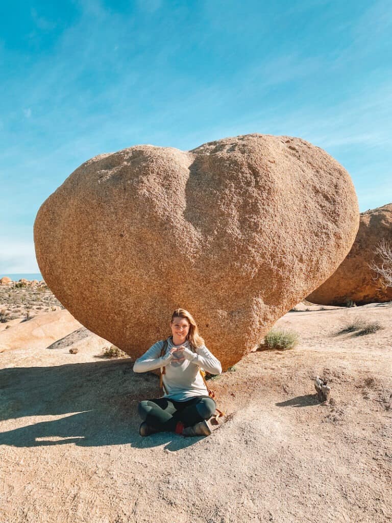 A hiker sits below a rock shaped like a giant heart in Joshua Tree.