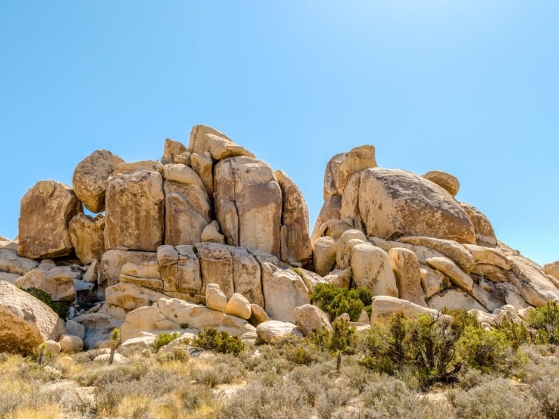 A large rock formation surrounded by scrub brush Joshua Tree. 