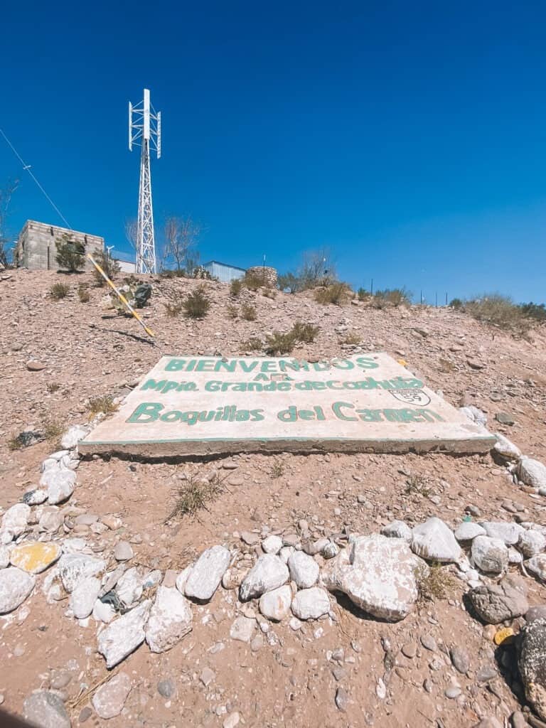 a white and teal hand painted sign weathered by the sign welcoming visitors to Boquillas del Carmen Mexico